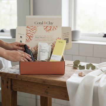 Lifestyle image featuring Coral & Clay For Yourself gift box on a rustic wooden table, filled with self-care items including a black pump bottle, a Fresh Fabulous Fig product, and a yellow-packaged item, styled with a white towel, eucalyptus leaves.