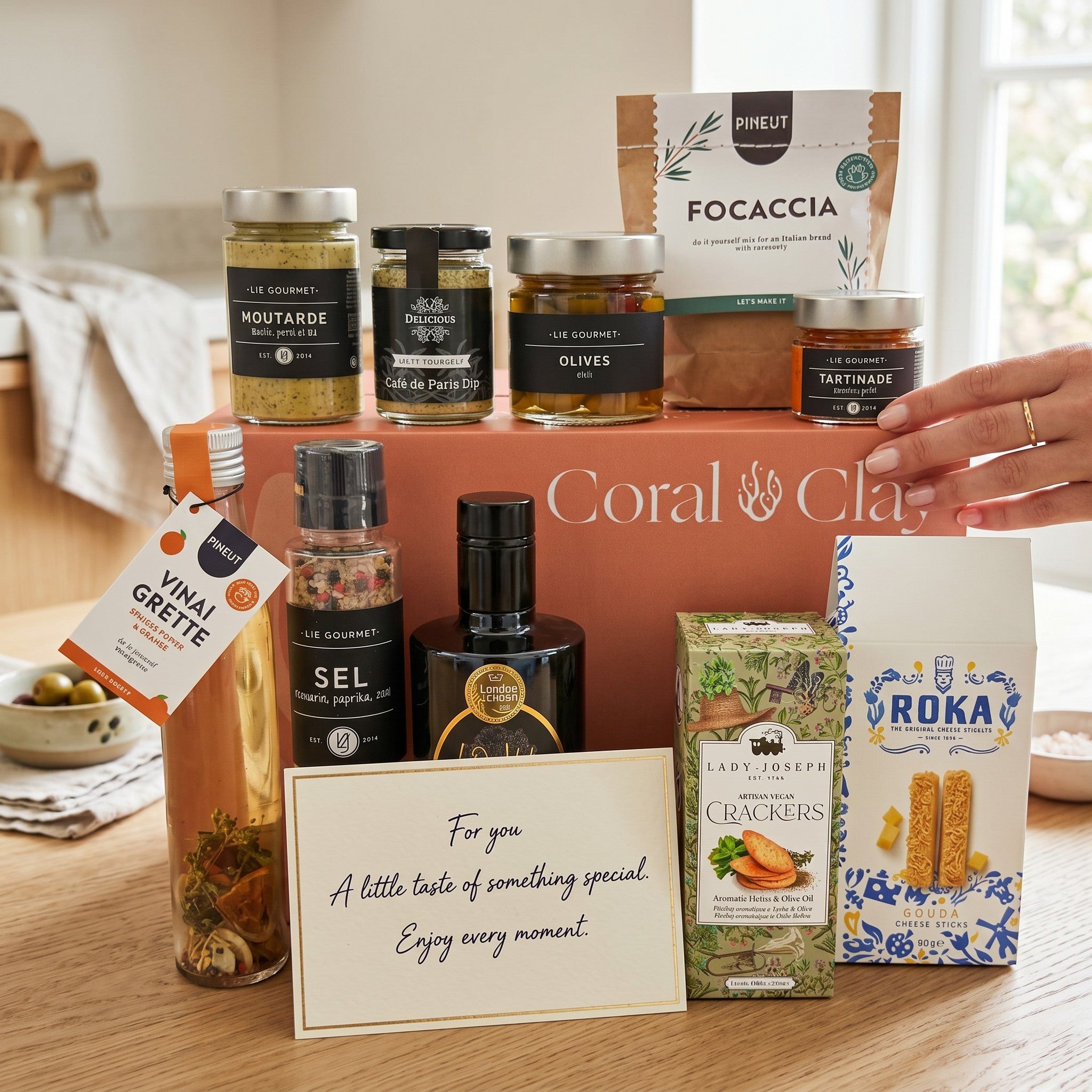 Coral & Clay Grand Gourmet gift set with various food items and a card on a wooden surface.
