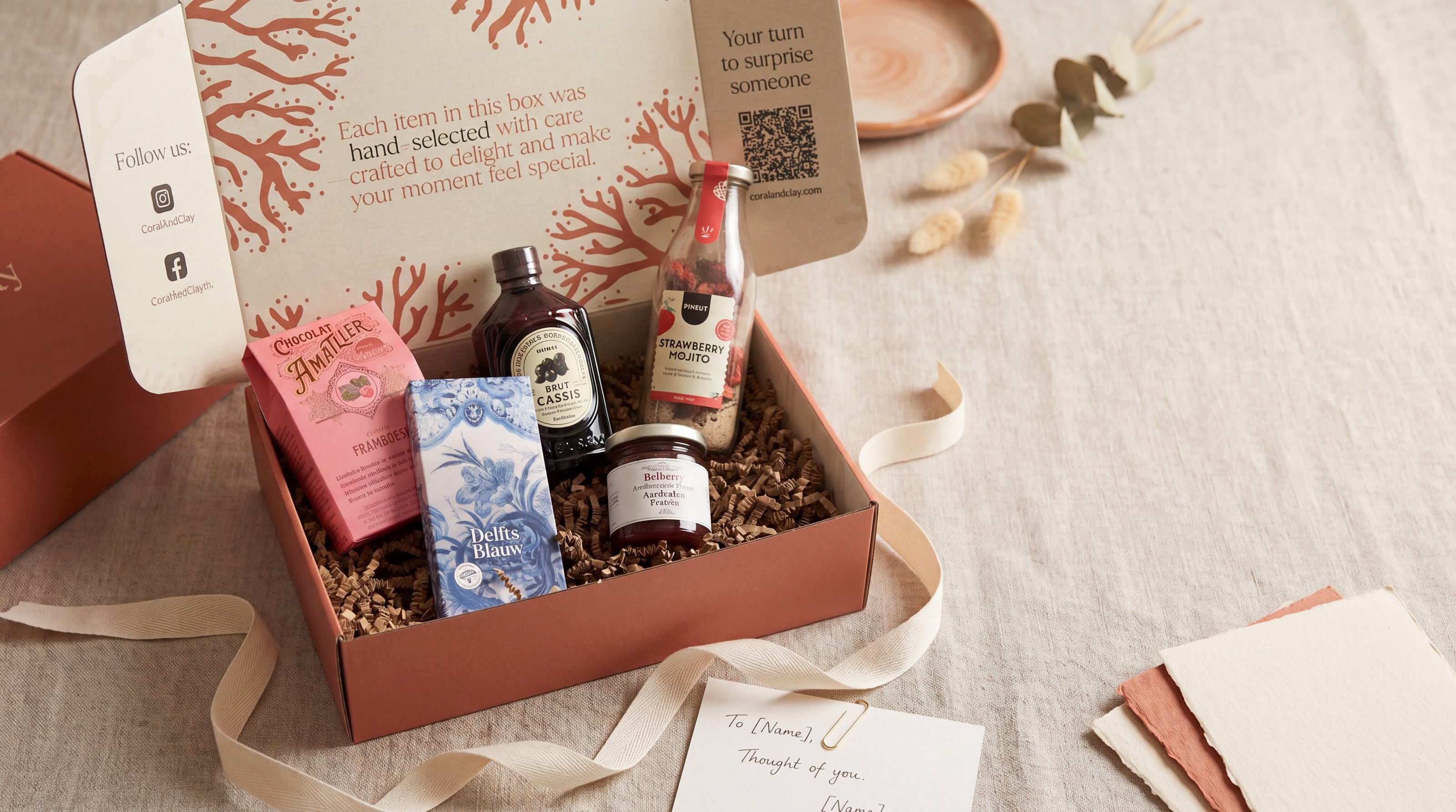 Coral & Clay gift box with various items including a bottle, soap, and jar on a textured surface.
