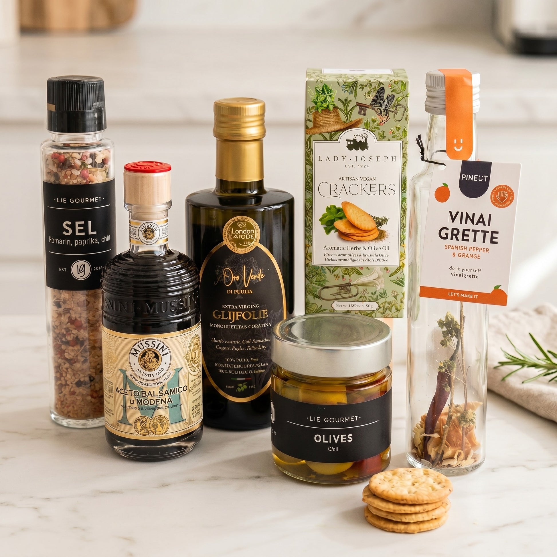 Assorted food products including olive oil, vinegar, olives, and crackers on a countertop.