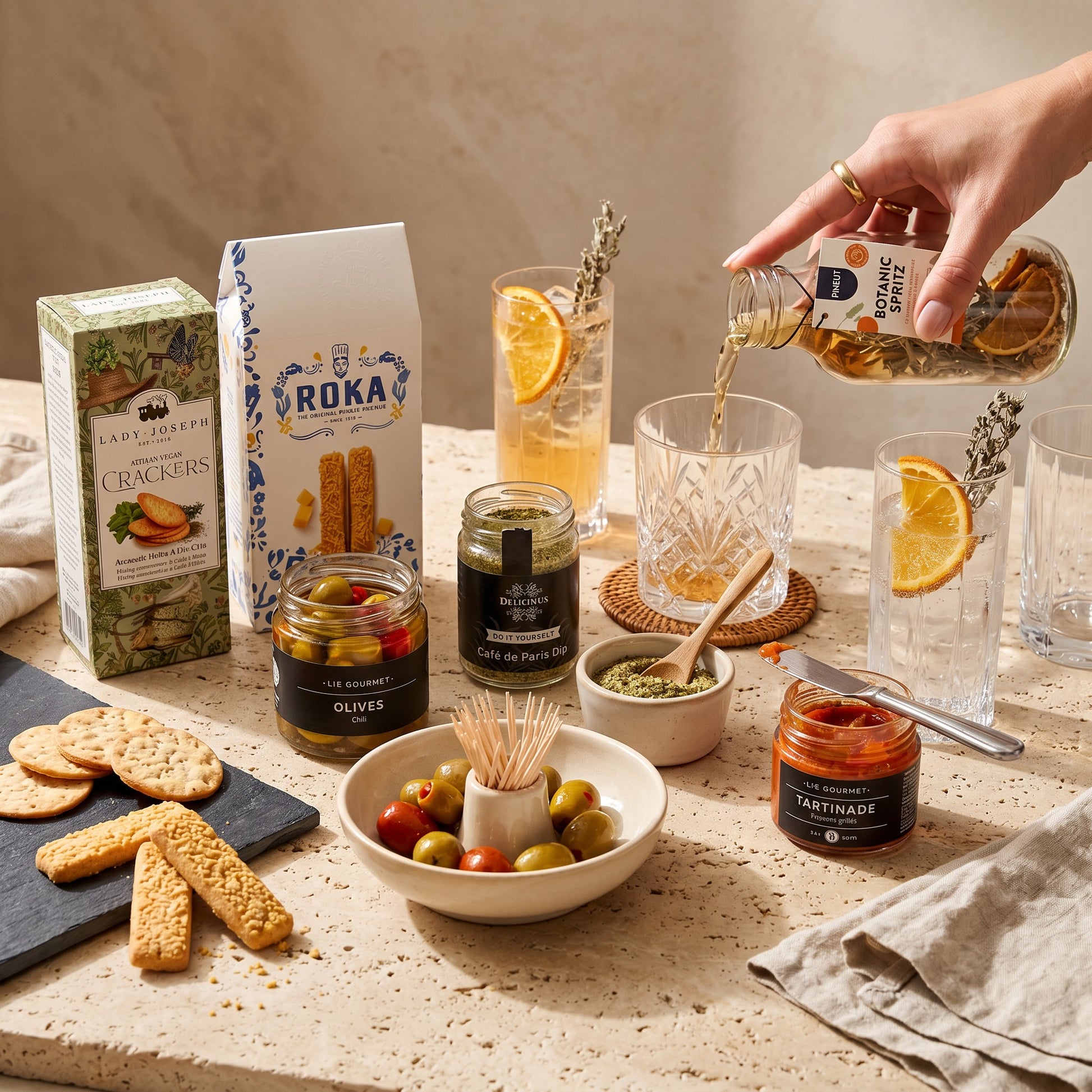 Table setting with snacks, drinks, and Roka crackers on a neutral background