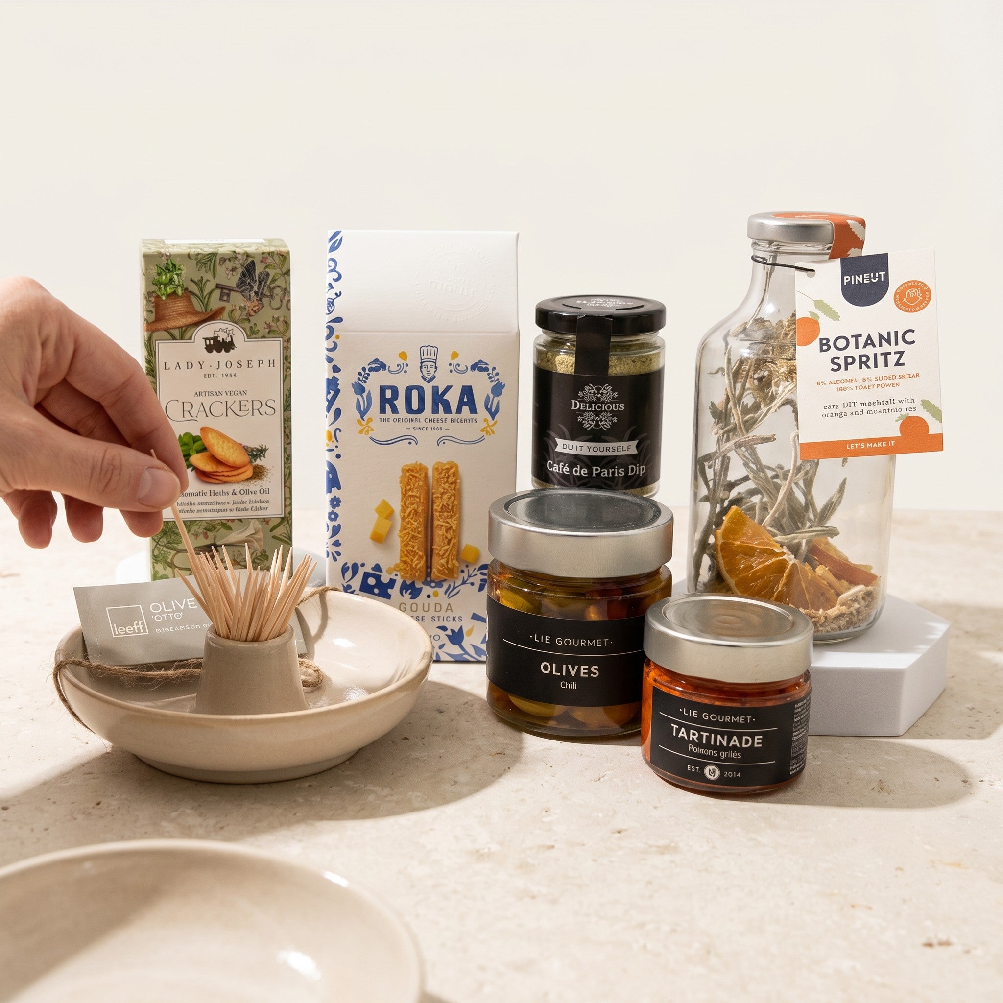 Assorted food items including crackers, olives, and tinned goods on a white surface.