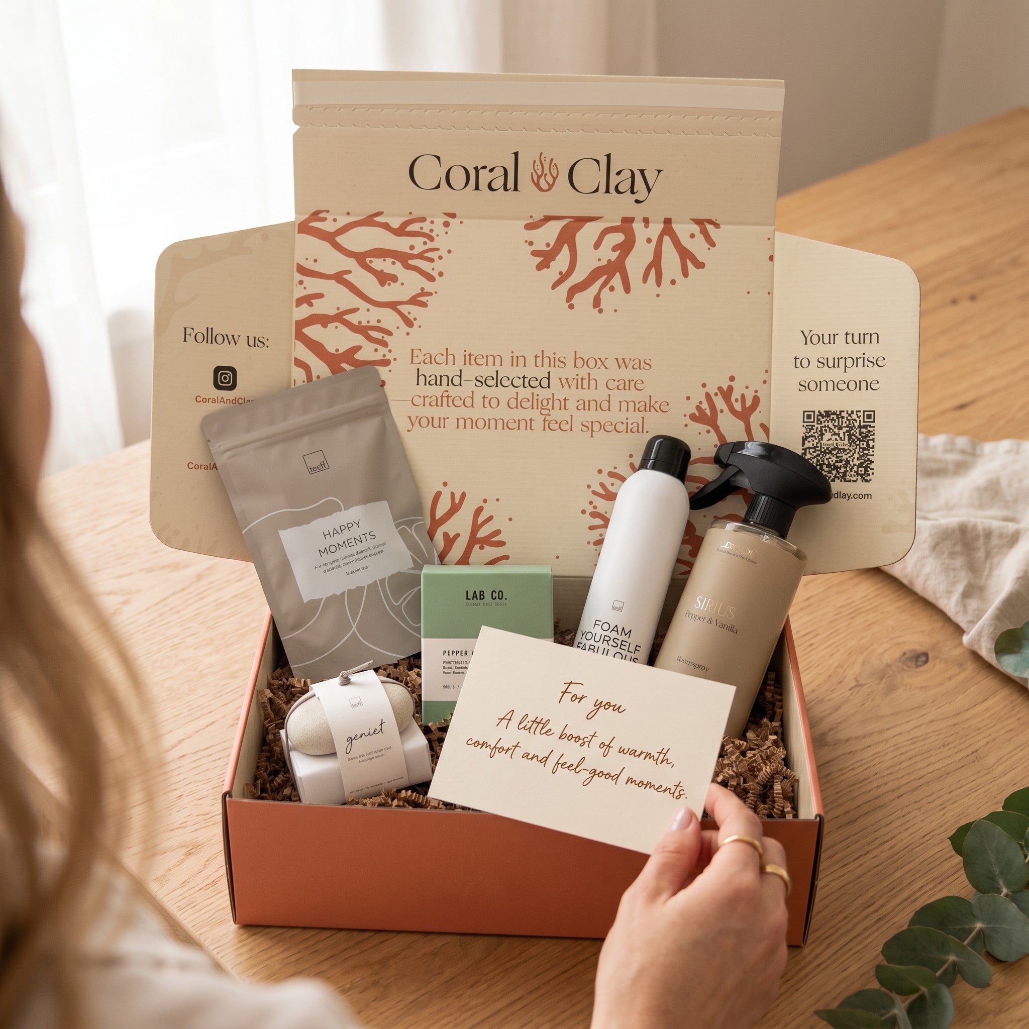 Gifting box with products and a card on a wooden surface, featuring the brand 'Coral Clay'.