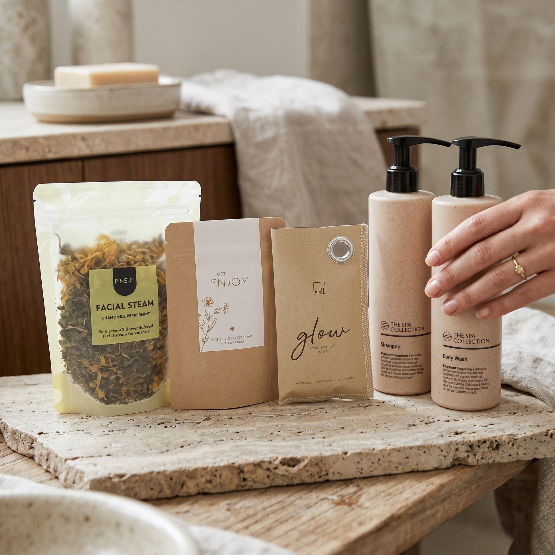 Home Spa Signature Gift bathroom setting with coffee scrub soap bar, chamomile peppermint facial steam, foot bath salts, Spa Collection body wash and shampoo on stone surface.