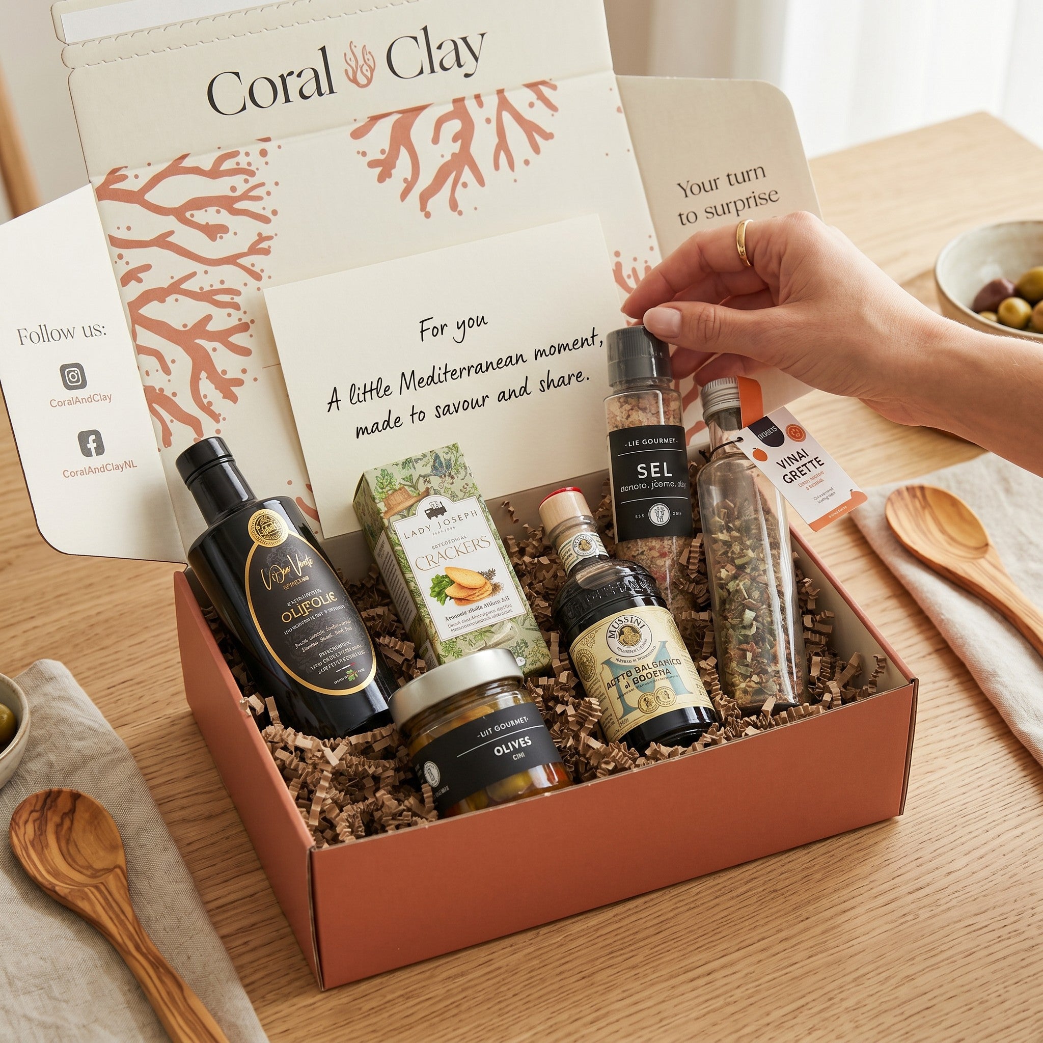 Gourmet gift box with various items including olive oil and herbs on a wooden table.