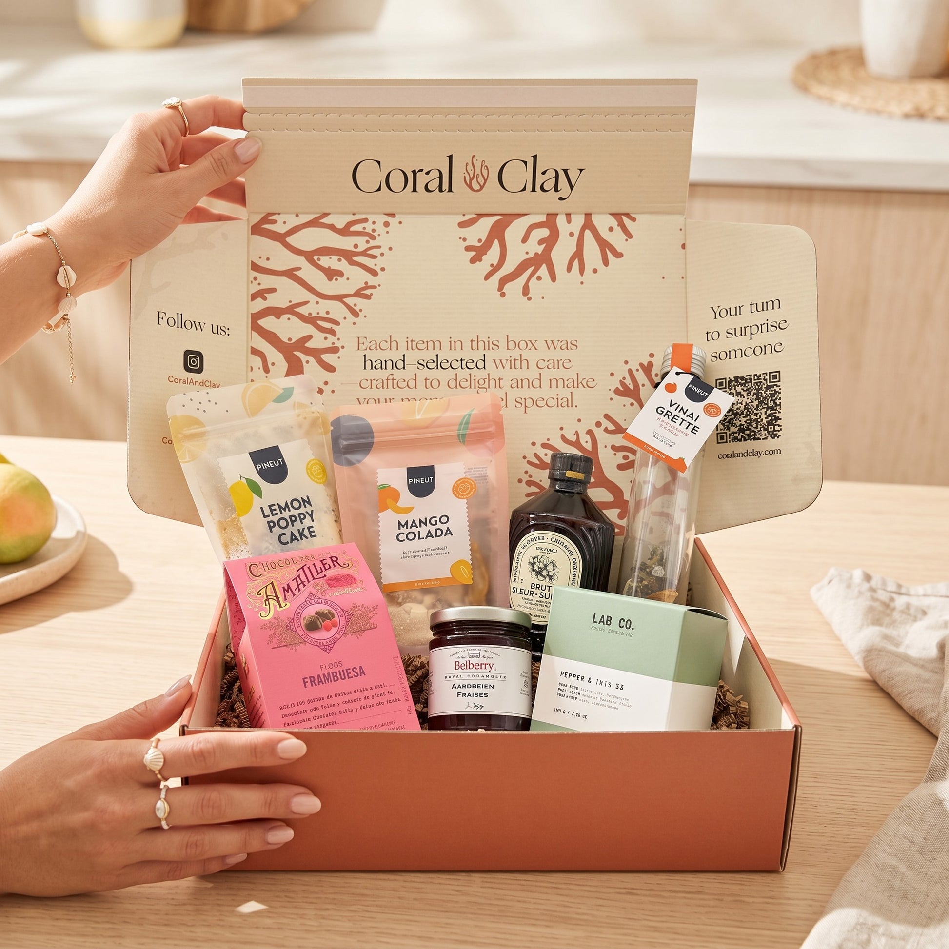 Coral & Clay Summer Feeling Signature Gift close-up lifestyle photo – wooden board with Mango Colada drink mix, elderflower syrup, lemon & poppy cake mix, strawberry confiture, raspberry pralines, Spanish pepper & orange vinaigrette, and scented candle.