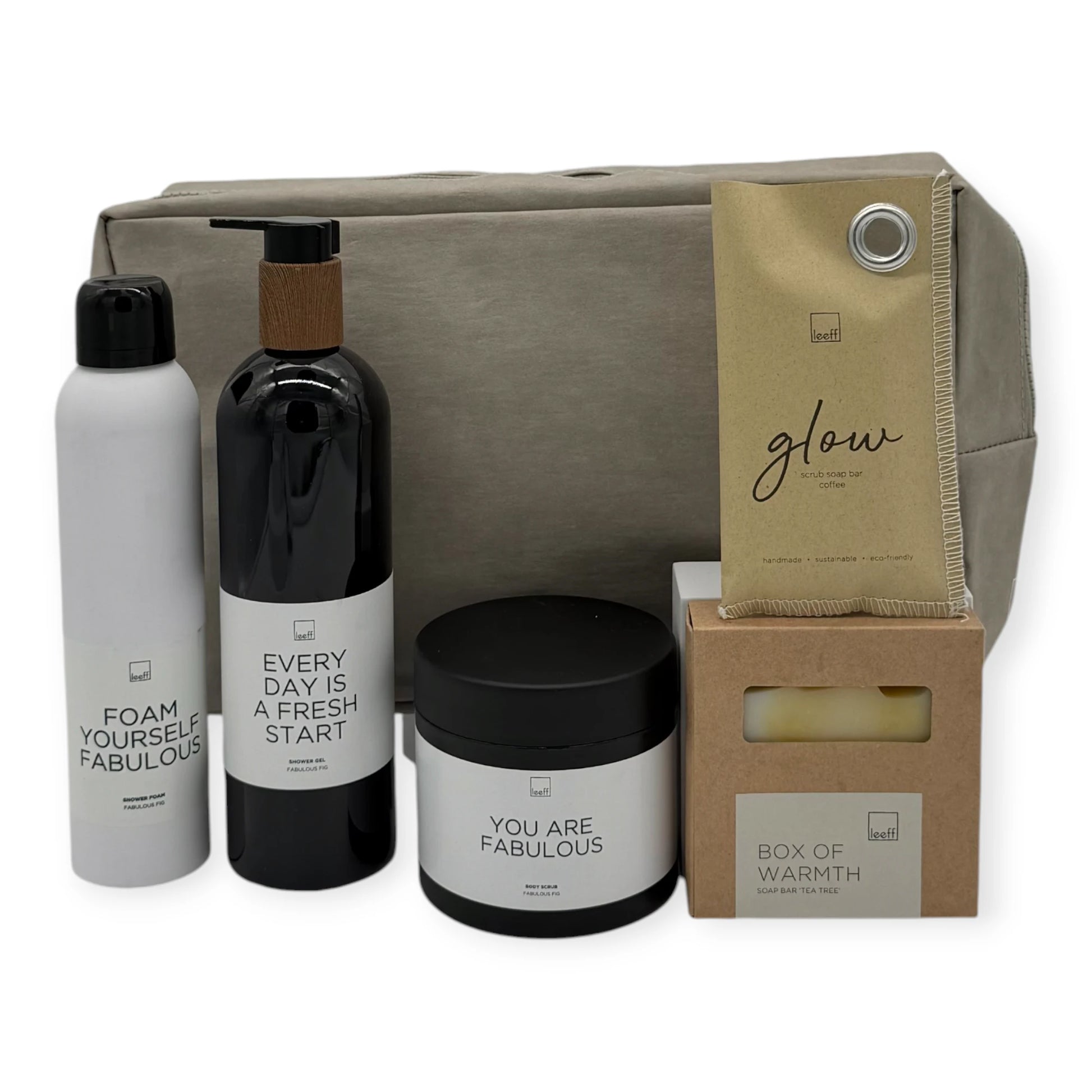 Grand Bath Retreat gift set contents including Leeff body foam, body scrub, hand soap, Glow scrub soap bar, Box of Warmth soap bar, and a large taupe toiletry bag.