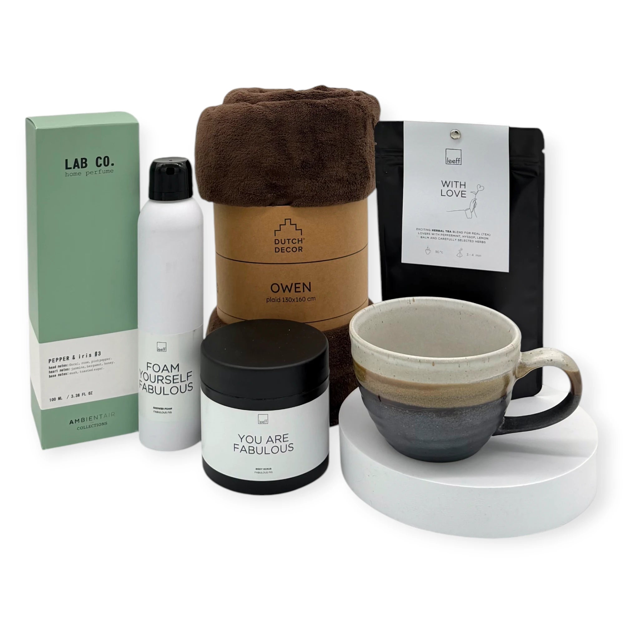 A curated selection of wellness essentials from the Coral & Clay Grand Body & Mind Gift Box, including a plush brown Dutch Decor Owen blanket, Leeff ‘With Love’ herbal tea, Leeff ‘Foam Yourself Fabulous’ shower foam, Leeff ‘You Are Fabulous’ body scrub, Lab Co. Pepper & Iris #3 home perfume, and a handcrafted ceramic mug in neutral tones.