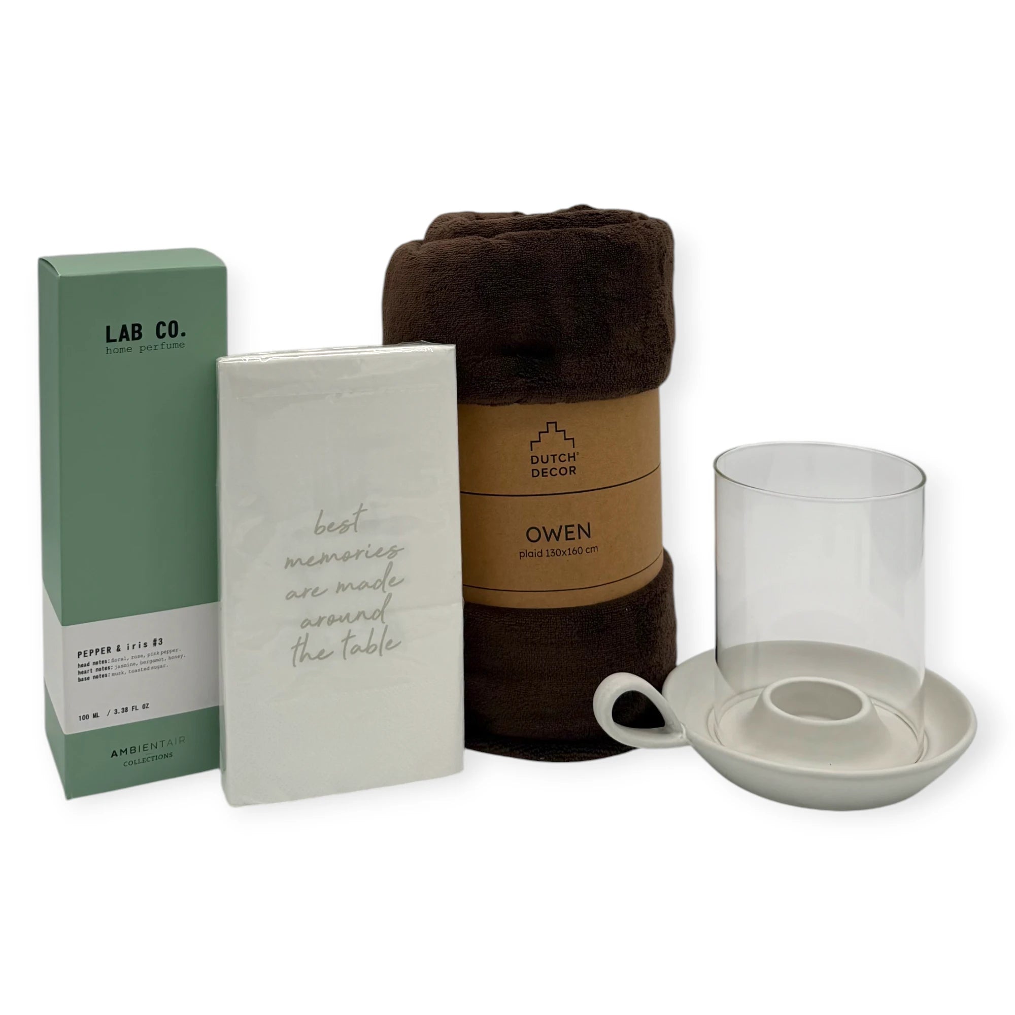 Image showing the contents of the Coral & Clay Hygge Grand Gift Box. The products include a mint-green LAB Co. home perfume (Pepper & Iris No.3), a pack of white napkins with the quote “best memories are made around the table,” a rolled dark-brown Dutch Decor Owen fleece blanket, and a ceramic candle holder with a clear glass hurricane cover. All items are arranged on a white background.