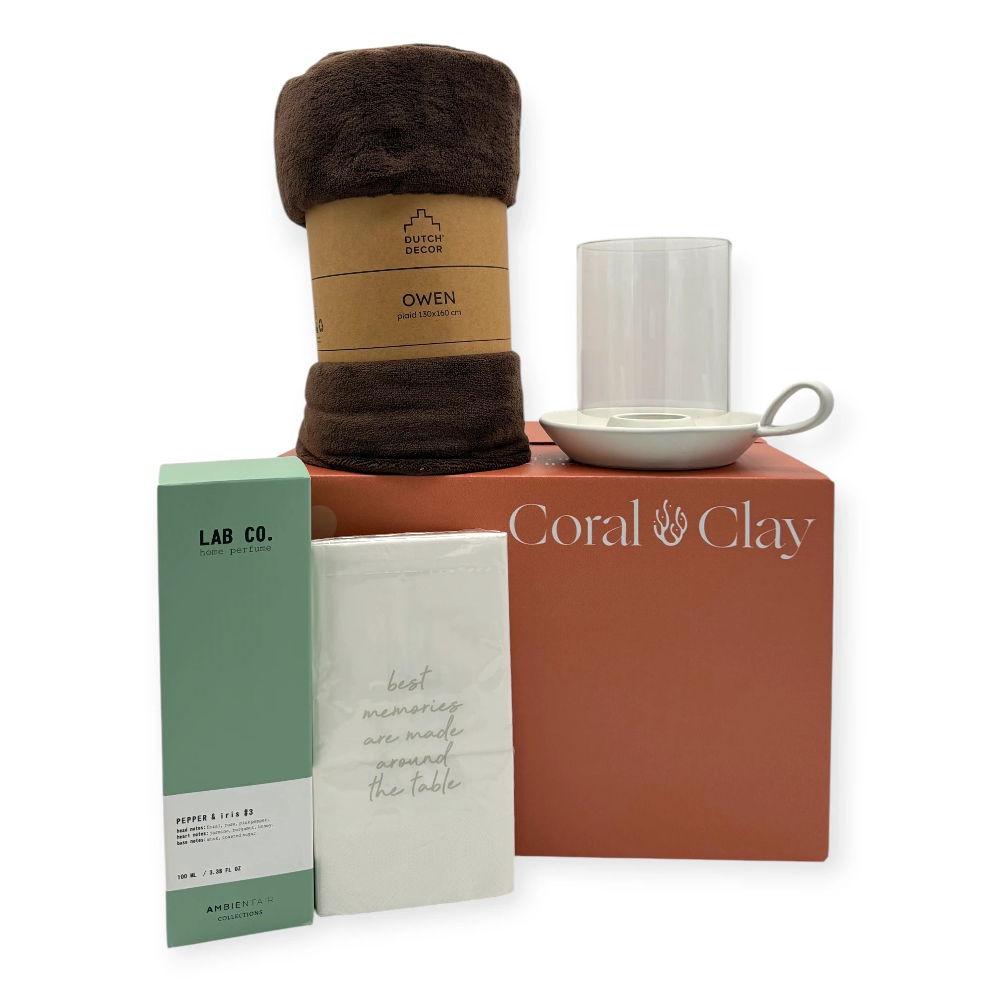 Lifestyle hero image of the Coral & Clay Hygge Grand Gift Box. The dark-brown Dutch Decor Owen fleece blanket is placed on top of the branded terracotta Coral & Clay gift box, alongside a ceramic candle holder with glass hurricane cover. In front of the box are the LAB Co. home perfume and white napkins with the printed quote. Clean, minimal styling emphasises cosy, hygge-inspired gifting.