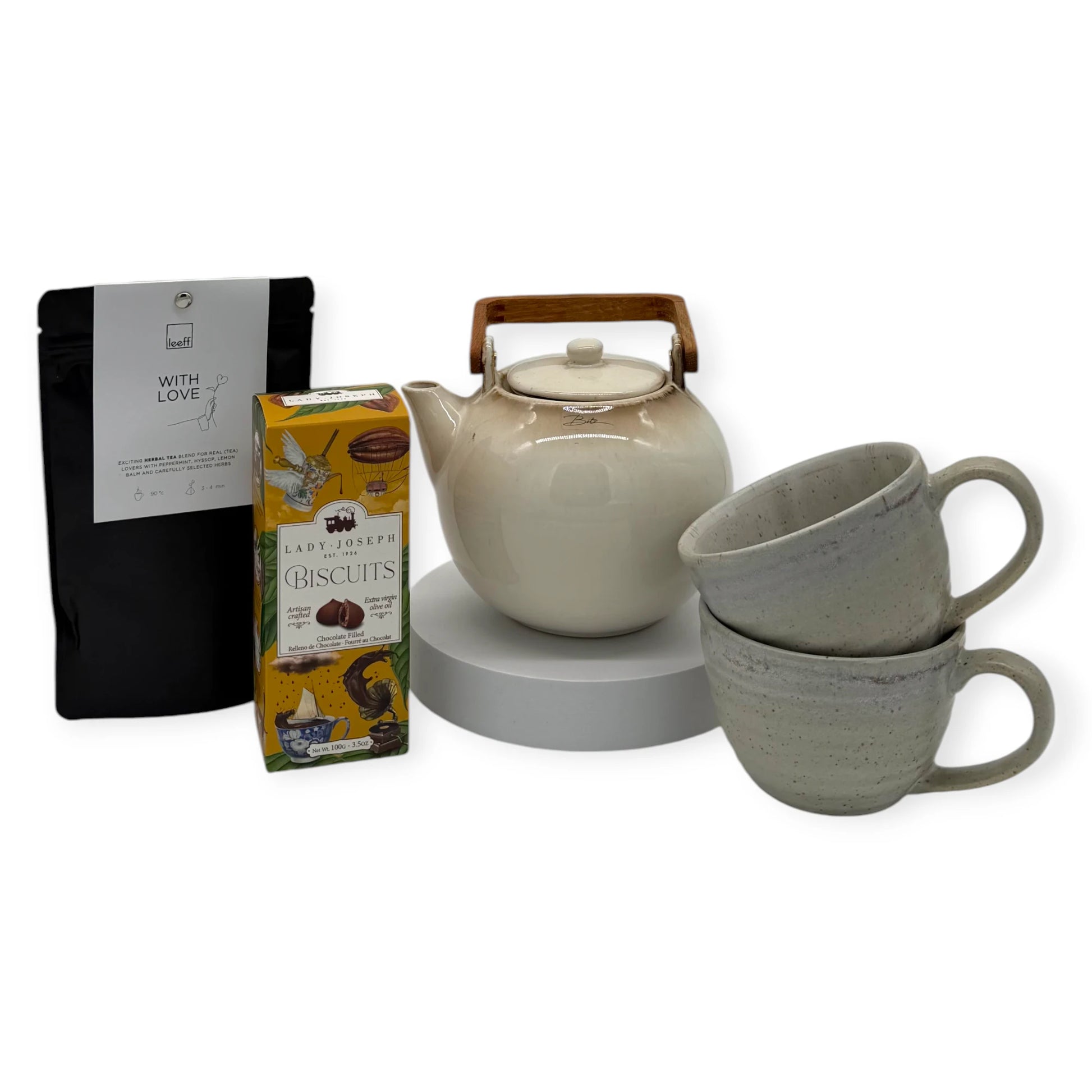 Grand Tea Ritual Gift Box contents arranged together: ceramic teapot with wooden handle, two stoneware mugs, Lady Joseph chocolate-filled biscuits, and Leeff ‘With Love’ loose-leaf herbal tea in black packaging.