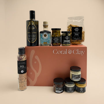 Coral & Clay Grand gift box filled with gourmet delicacies, including extra virgin olive oil, balsamic vinegar, artisanal pasta, flavored salts, and assorted tapenades. The coral-inspired box serves as a backdrop for an indulgent Mediterranean spread.”