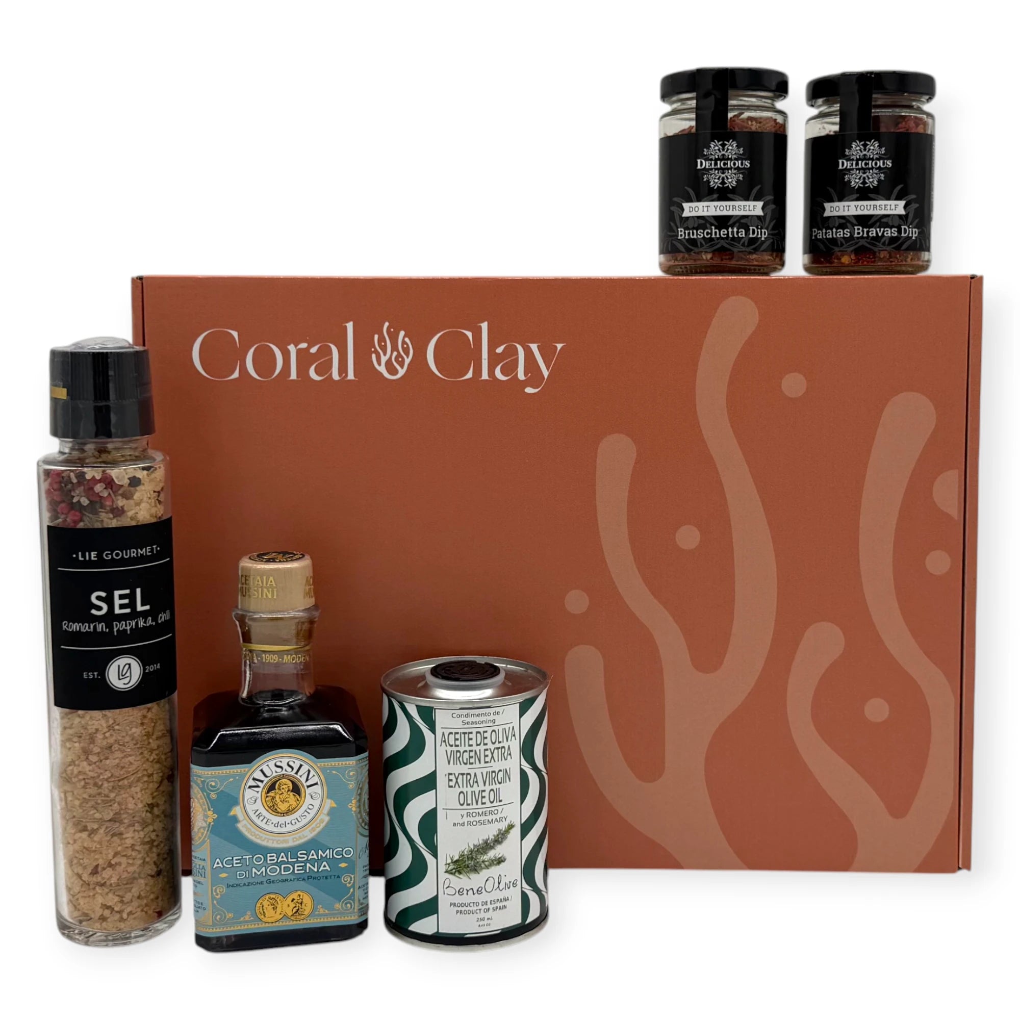 Gourmet cooking ingredients displayed in front of a Coral & Clay signature gift box, including Lie Gourmet seasoned salt, Mussini balsamic vinegar, Beneoliva rosemary extra-virgin olive oil, and two Delicious dip jars.