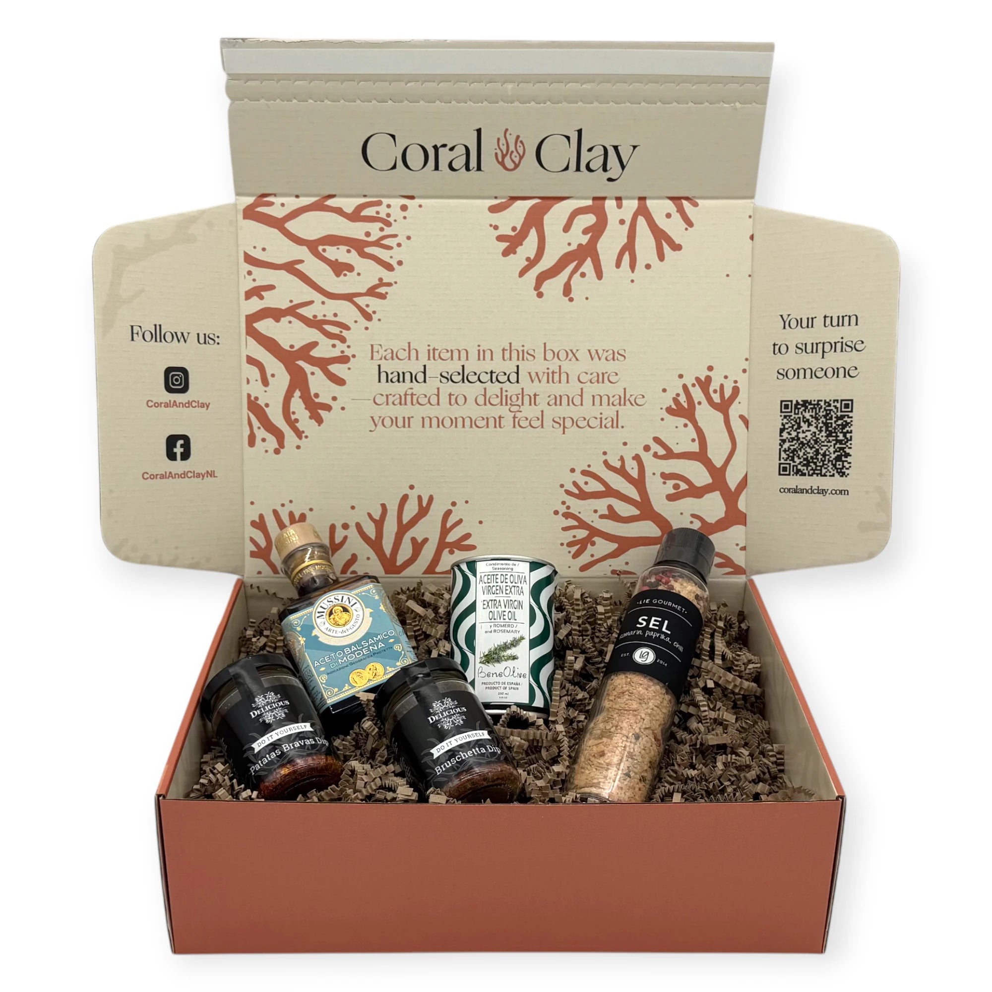 Open Coral & Clay gift box filled with gourmet cooking items nestled in kraft filler: Lie Gourmet seasoned salt grinder, Mussini Modena balsamic vinegar, Beneoliva rosemary olive oil tin, and two Delicious dip jars.