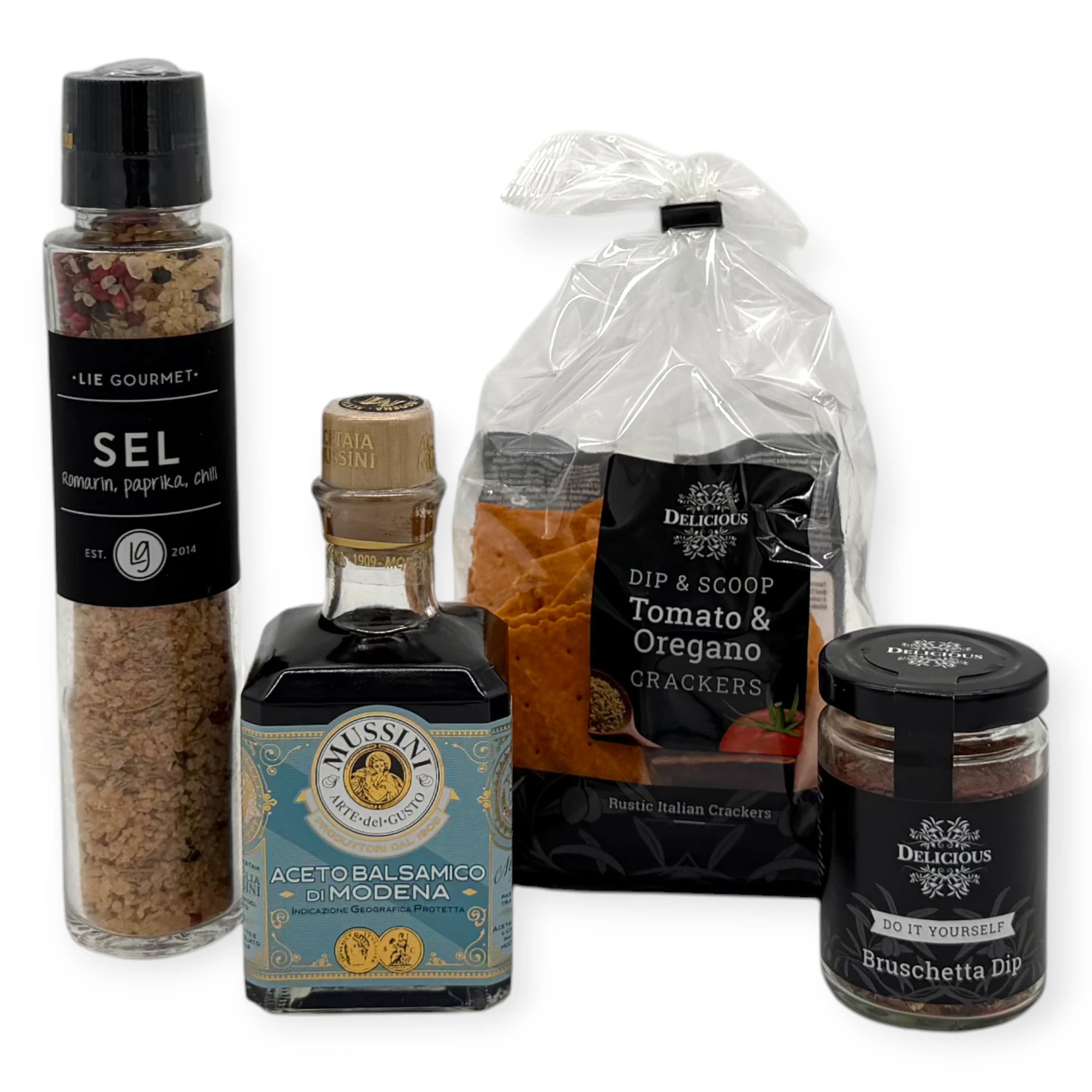 Assorted gourmet cooking essentials including Lie Gourmet rosemary paprika chili salt grinder, Mussini Aceto Balsamico di Modena, Benolive rosemary olive oil tin, and two Delicious Do-It-Yourself dips (Bruschetta and Patatas Bravas).