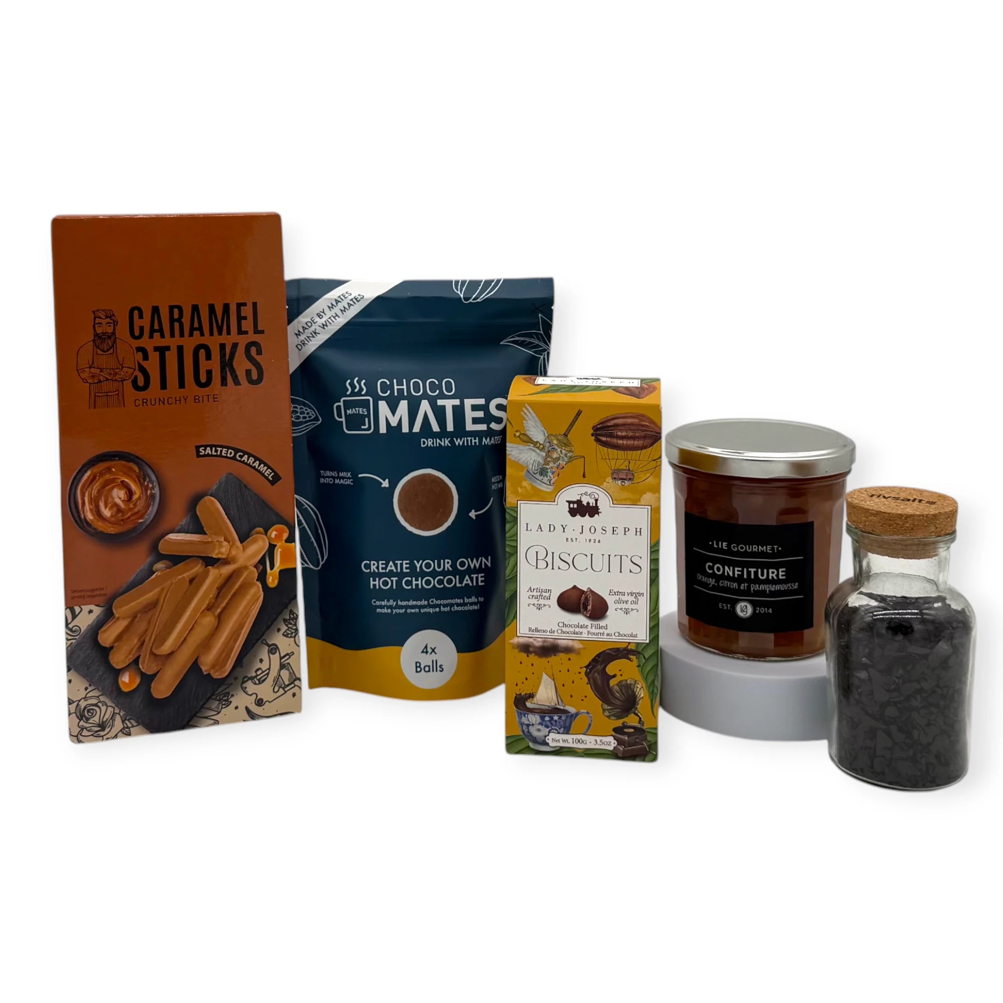 A curated selection of sweet treats from the Sunday Afternoon Signature Gift, including caramel sticks, hot chocolate mix, chocolate-filled biscuits, a jar of fruit confiture, and a small bottle of decorative chocolate flakes arranged together against a white background.