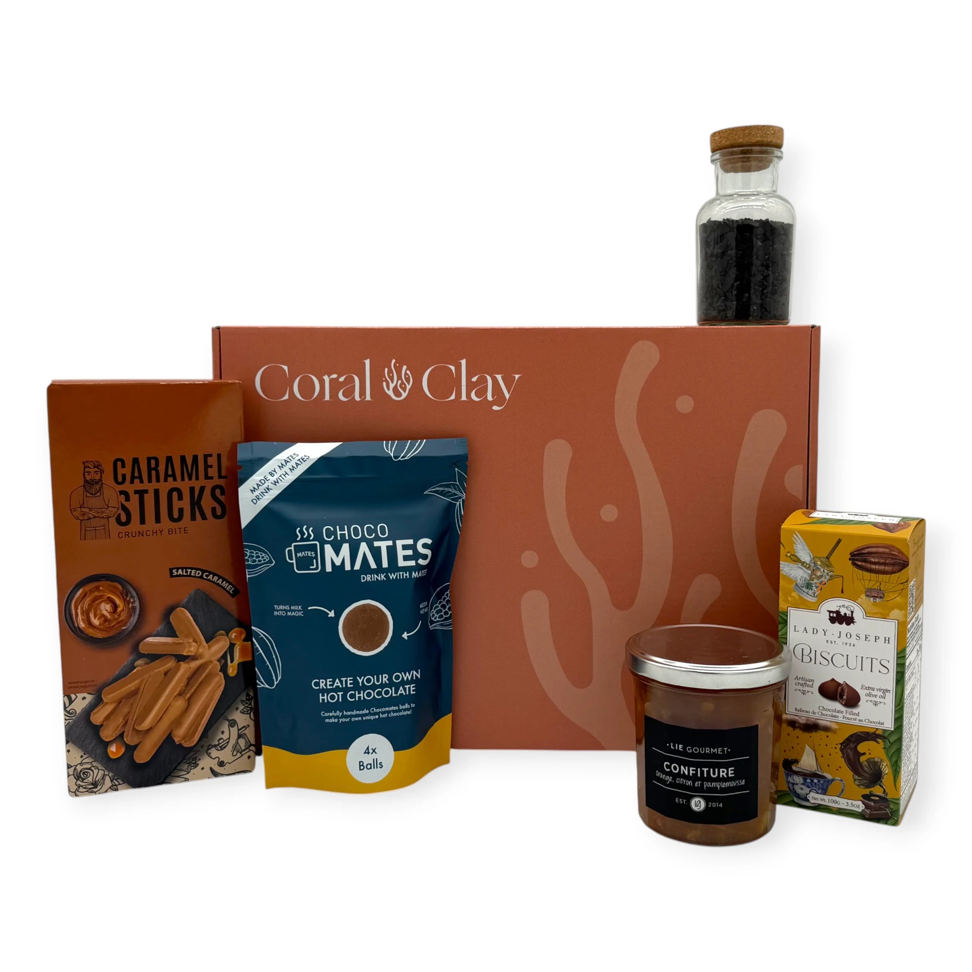 The Sunday Afternoon Signature Gift displayed in front of a Coral & Clay gift box, featuring caramel sticks, hot chocolate mix, chocolate-filled biscuits, fruit confiture, and a small bottle of chocolate flakes arranged neatly for a hero product shot.