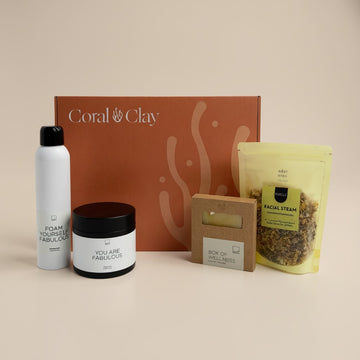 Coral & Clay Signature gift box displayed against a neutral background, featuring luxury self-care items including a foaming cleanser, body cream, facial steam pouch, and a wellness soap bar. The elegant coral-themed box adds a premium touch.
