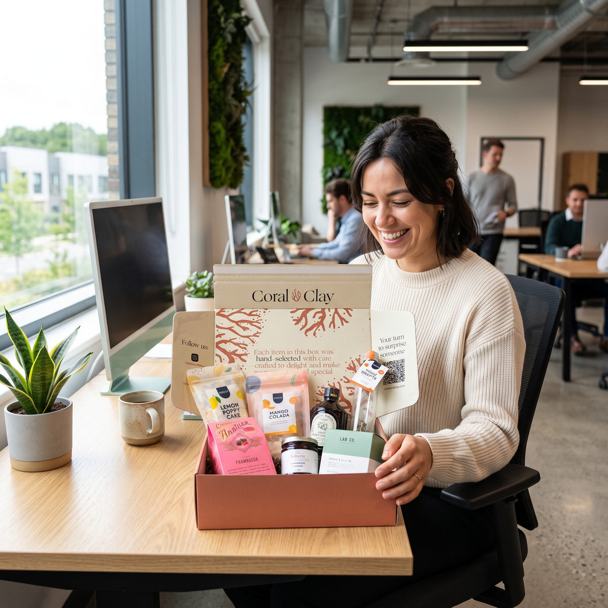 Woman opening a Coral & Clay corporate gifting employee gift box with chocolate, cake mix, drinks and treats at her office desk